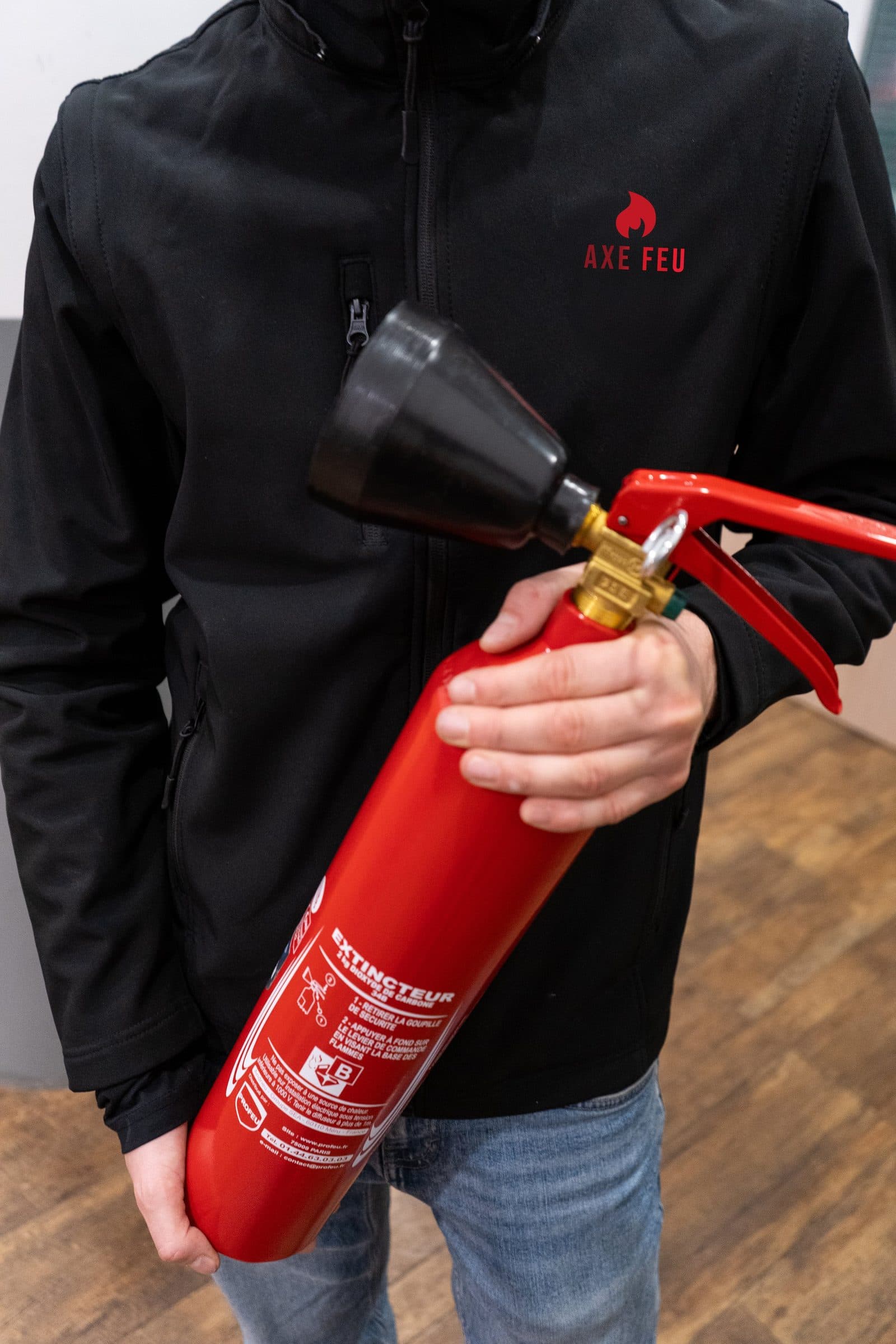 Technicien AXE FEU en veste floquée présentant un extincteur CO₂ à installer en Île-de-France