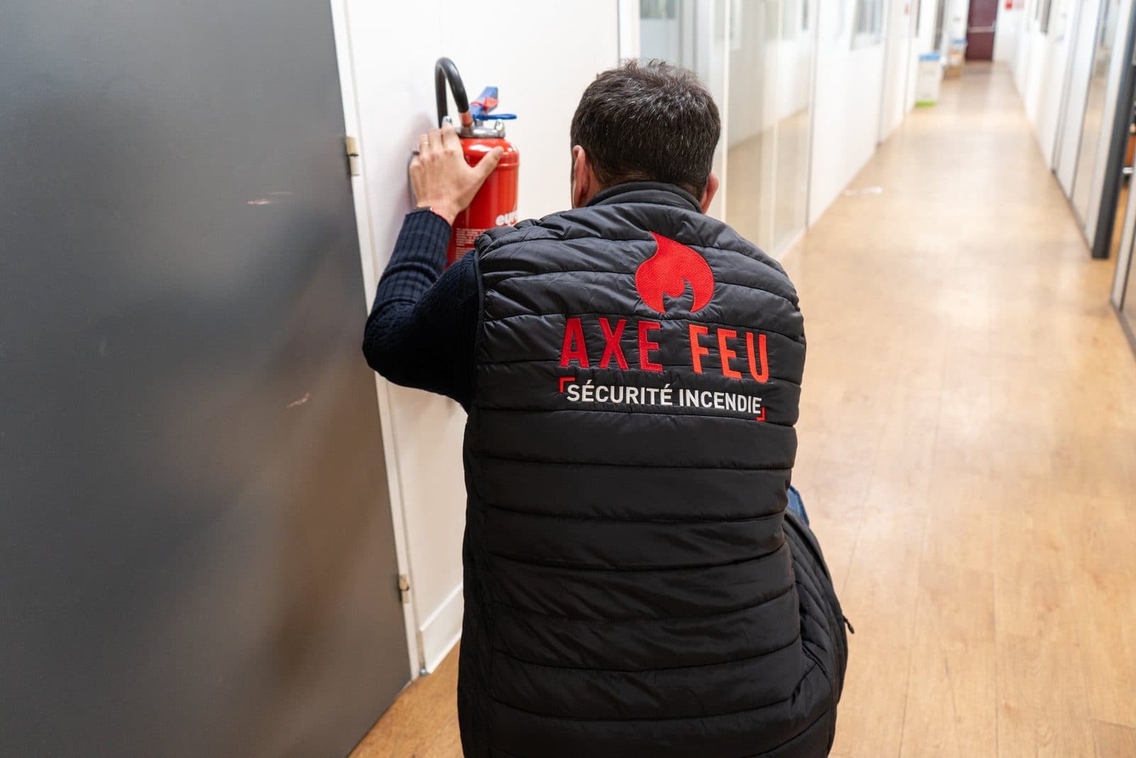 Technicien AXE FEU réalisant la maintenance d'un extincteur dans un couloir d'entreprise en Essonne